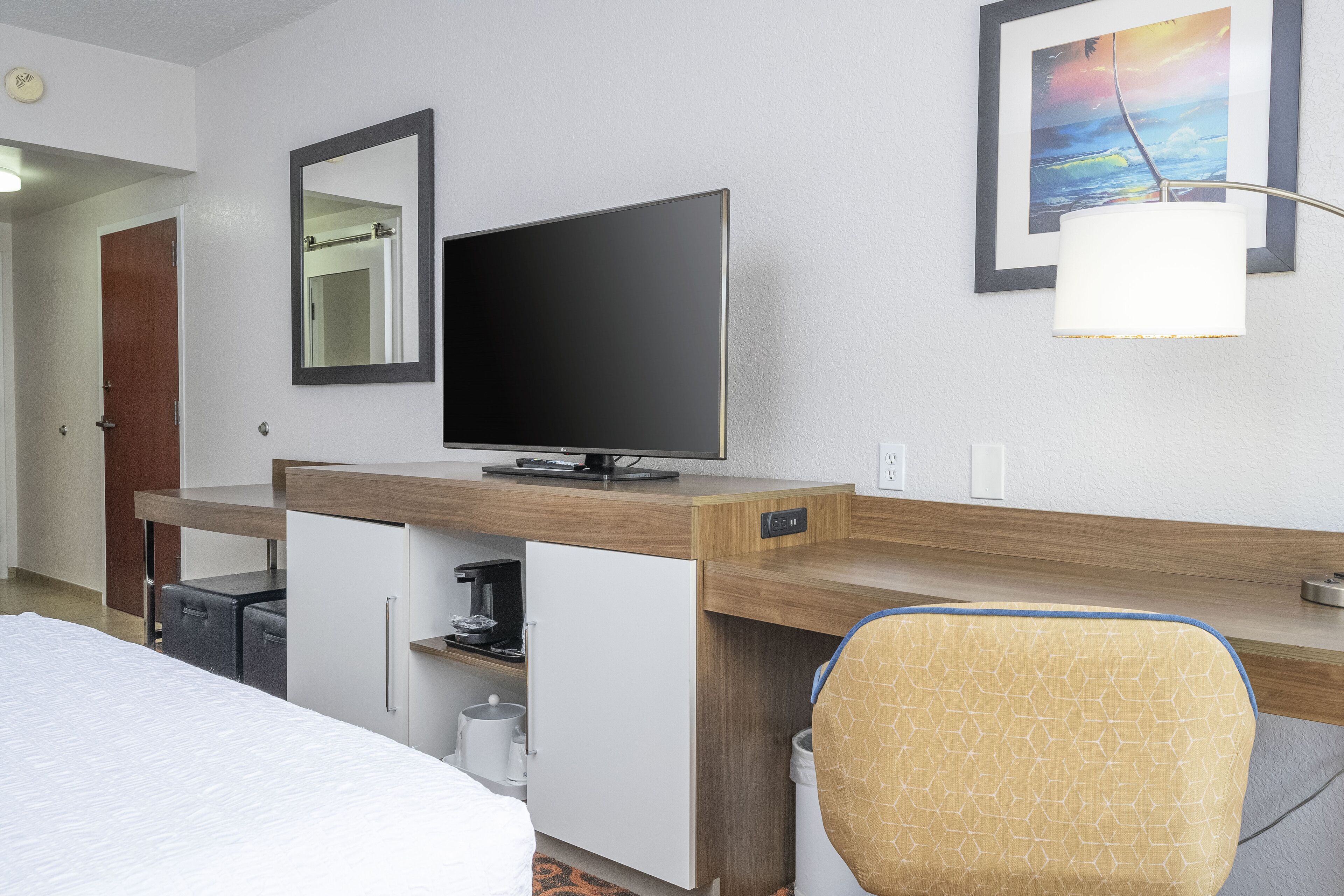 Ein Hotelzimmer mit einem Bett, einem Schreibtisch mit Fernseher, einem Sessel und einem Bild an der Wand.