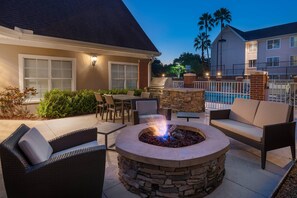 An outdoor patio with a stone fire pit, wicker furniture, and a pool area.