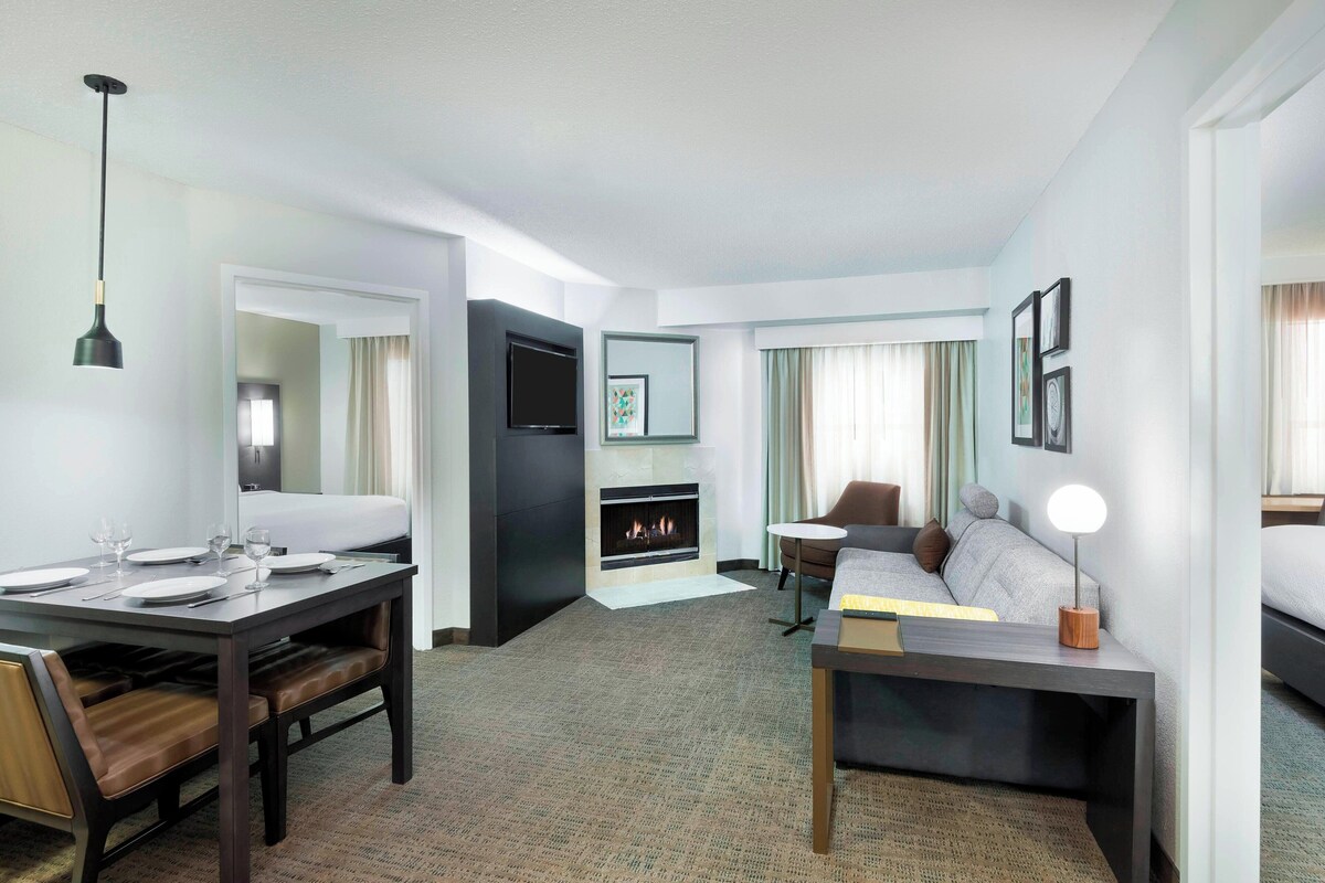 Una habitación de hotel con una mesa de comedor, un sofá, un televisor, una chimenea y una cama.
