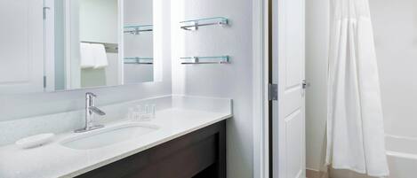 A modern bathroom with a white sink, a mirror, and a glass shelf.