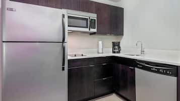 Uma cozinha compacta com geladeira, micro-ondas, cafeteira e lava-louças.