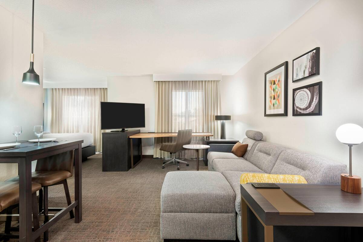 Una habitación de hotel moderna con sofá, escritorio, televisor y zona de comedor.