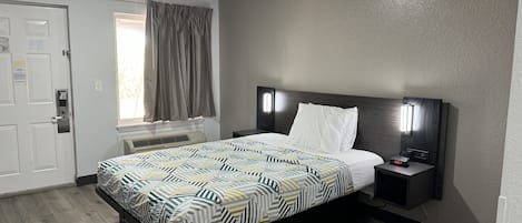 A hotel room with a bed, bedside table, nightstand, and a window with curtains.