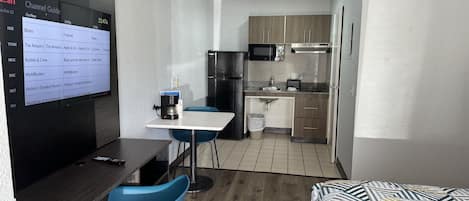 Habitación de hotel compacta con kitchenette, zona de comedor con mesa y sillas azules, y cama con edredón estampado.