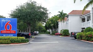 Ein Studio 6 Hotel für Langzeitaufenthalte mit Parkplatz, Bäumen und einem Gebäude mit roter Ziegeldach.