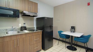 Eine kompakte Küche mit Holzausbau, einem schwarzen Kühlschrank, einer Mikrowelle, einer Kaffeemaschine und einem kleinen Tisch mit blauen Stühlen.