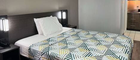 A hotel room with a neatly made bed, a bedside table with a phone, and a nightstand with a lamp.