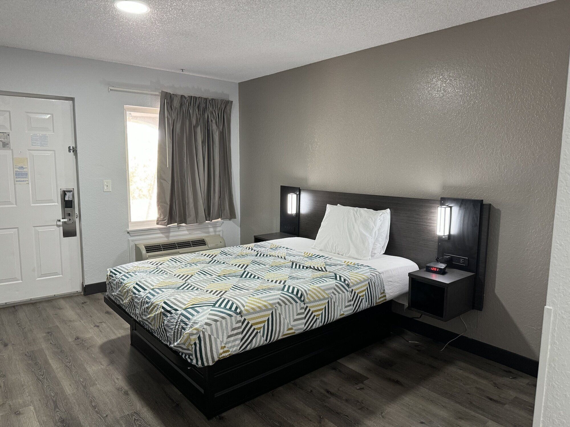 A hotel room with a bed, bedside table, and a window with curtains.