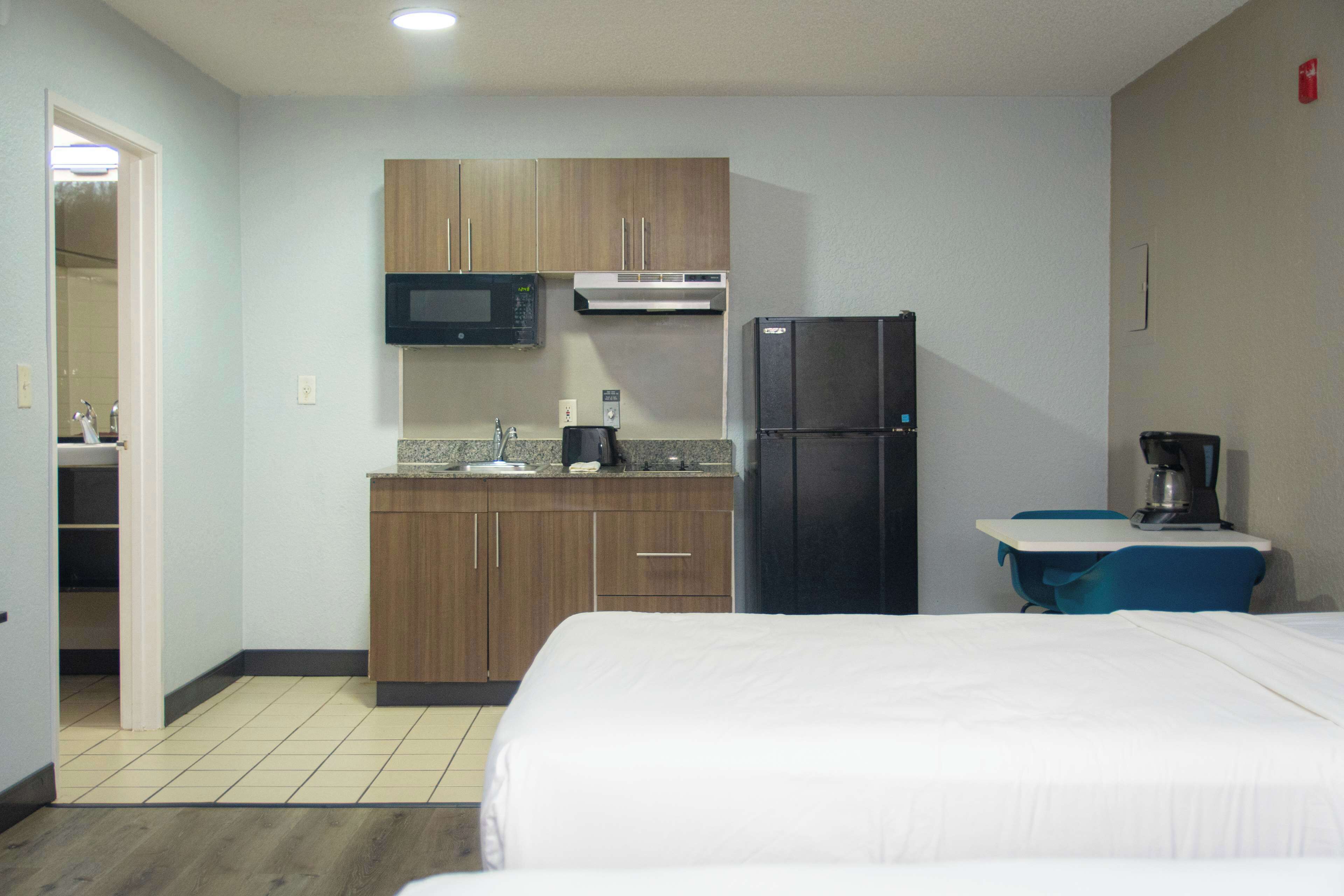 Une chambre d’hôtel comprenant un lit, une kitchenette équipée d’un four à micro-ondes, d’un réfrigérateur et d’un évier, ainsi qu’une petite table avec une chaise.