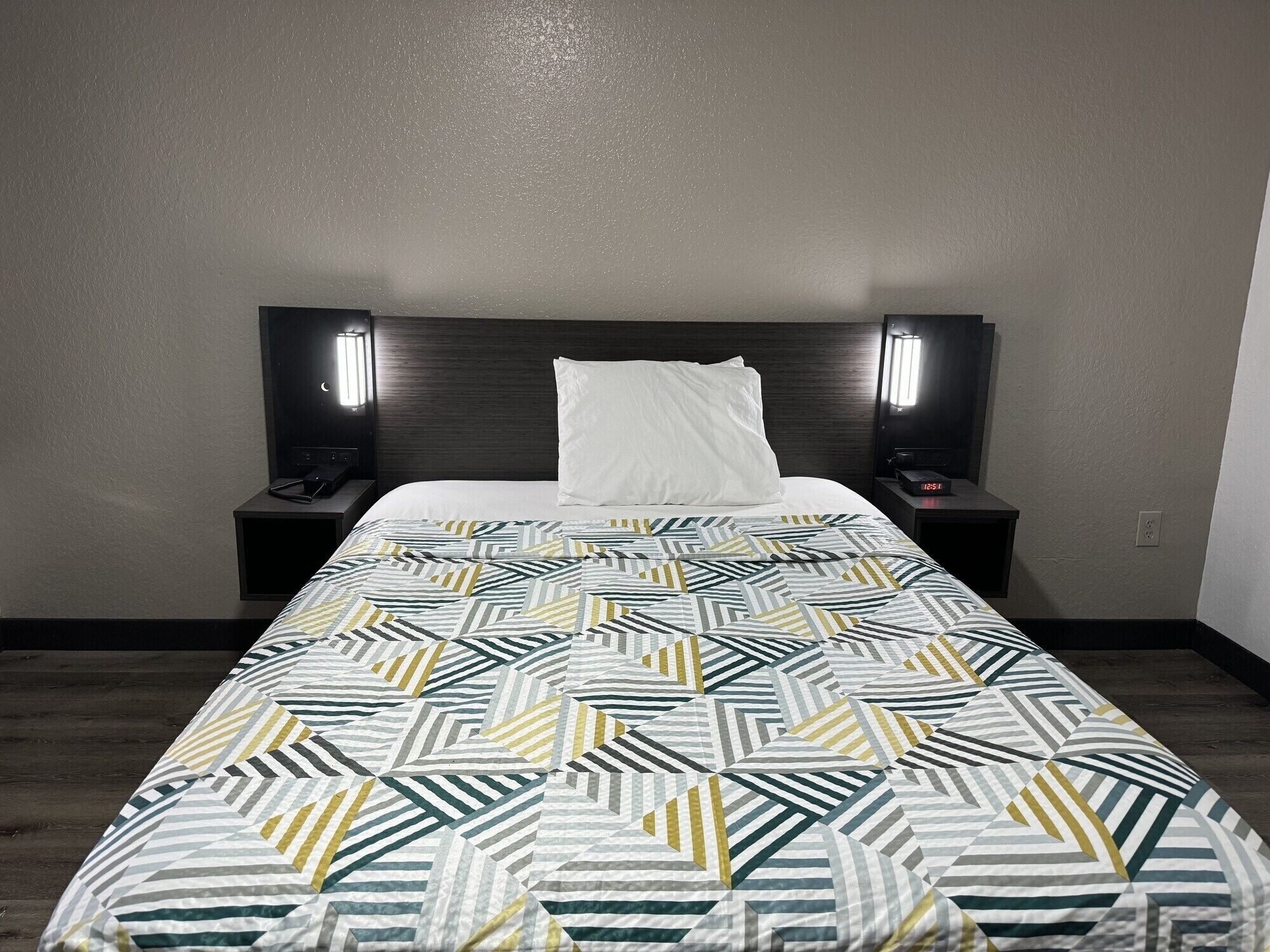 A hotel room with a bed, two bedside tables, and two wall-mounted lamps.