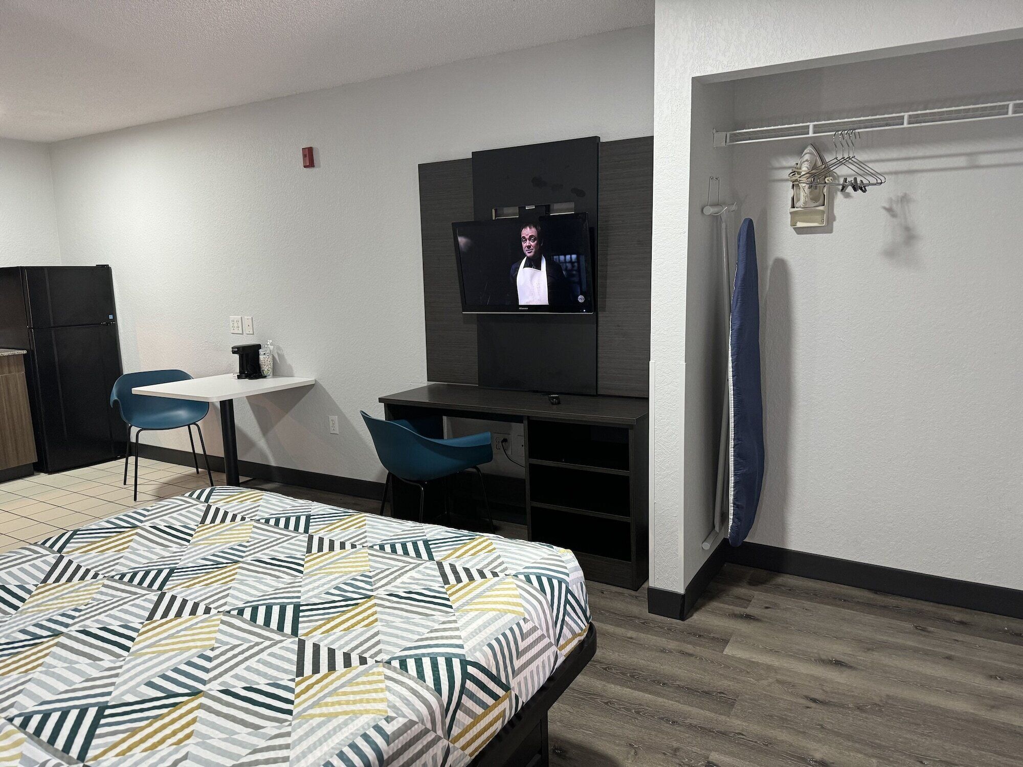 A hotel room with a bed, a desk, a chair, a television, and a surfboard.
