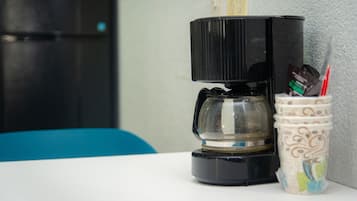 En kaffebryggare står på ett vitt bord bredvid en kopp med sugrör och en sked.