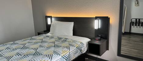 Una habitación de hotel con una cama, mesitas de noche, una lámpara de pared y un espejo.