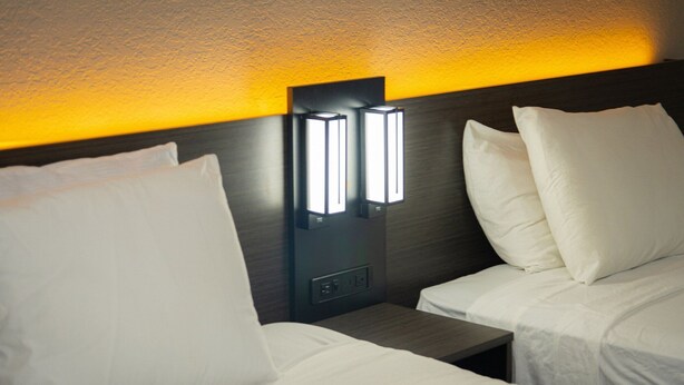 Ein Hotelzimmer mit zwei Betten, jeweils mit weißer Bettwäsche und Kissen. Über den Betten befindet sich eine Wandleuchte.