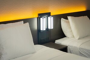 A hotel room with two beds, each with white bedding and pillows. There is a wall-mounted light fixture above the beds. - Studio 6 Extended Stay - West Palm Beach, FL (West Palm Beach)