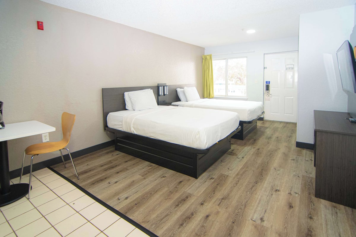 A hotel room with two beds, a desk, a chair, and a television.