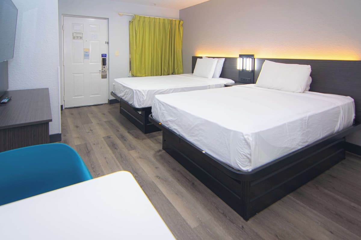 A hotel room with two beds, a desk, and a chair.