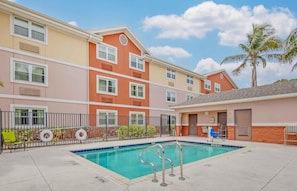 A hotel with a swimming pool, multiple balconies, and a palm tree.