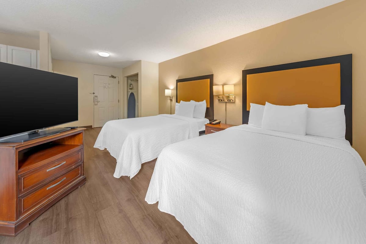 Ein Hotelzimmer mit zwei Betten, einem Fernseher, einer Holzkommode und einer Tür.