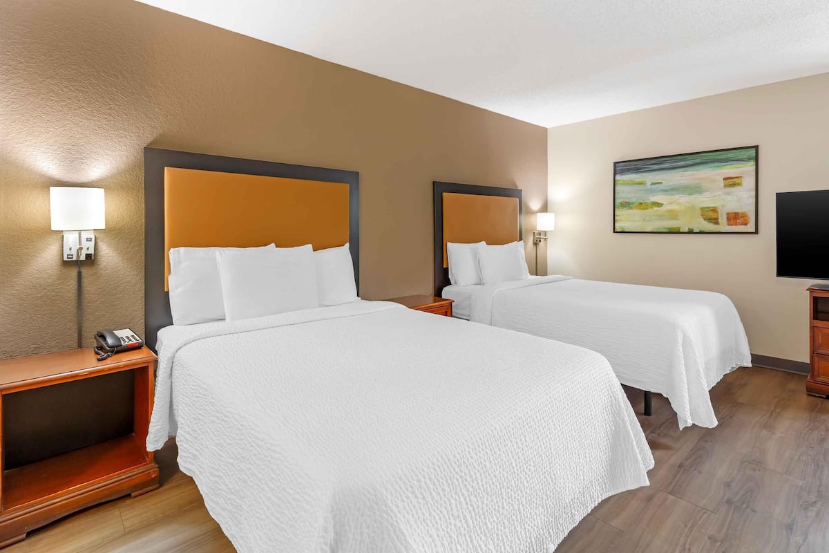 Ein Hotelzimmer mit zwei Betten, einem Fernseher, einem Gemälde und einem Telefon auf dem Nachttisch.