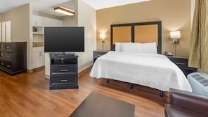 A hotel room with a bed, bedside tables, a TV, a desk, and a kitchenette.
