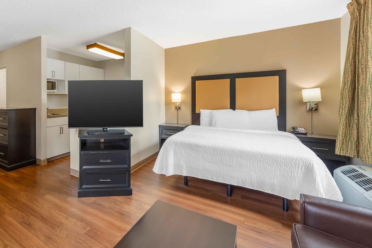 Ein Hotelzimmer mit Bett, Nachttischen, Fernseher, Schreibtisch und einer Küchenzeile.