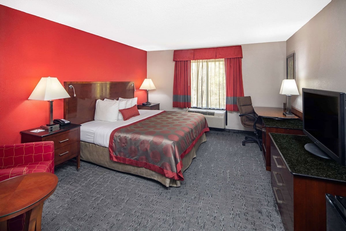 A hotel room with a bed, two bedside tables, a desk with a chair, a television, and a window with curtains.