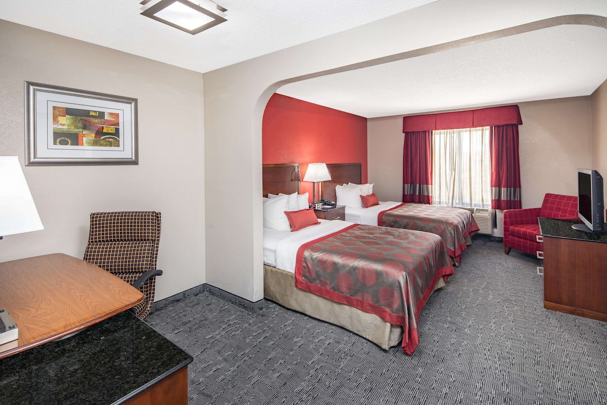 A hotel room with two beds, a desk, a chair, and a TV.