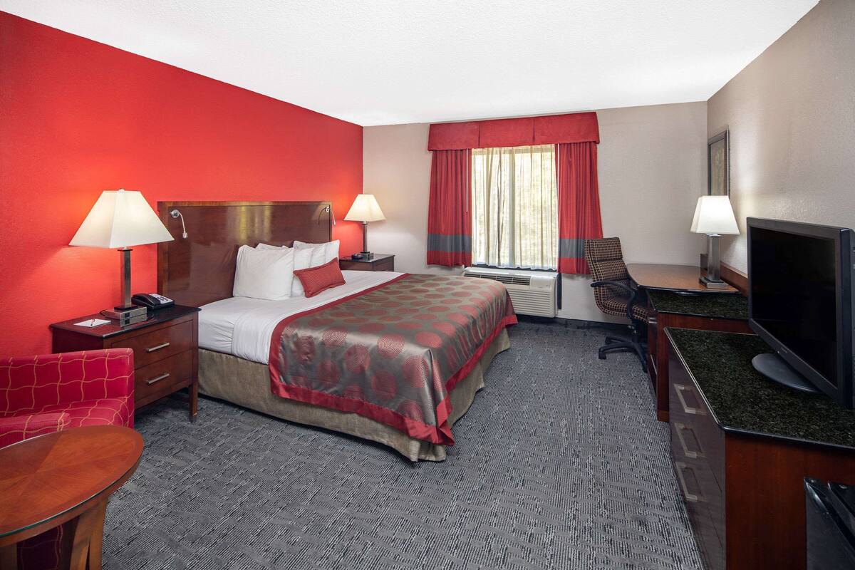 A hotel room with a bed, two bedside tables with lamps, a desk with a television, a chair, and a carpeted floor.