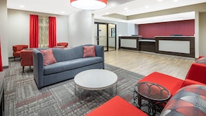 A modern lobby with a grey sofa, red accents, a round coffee table, and a reception desk. - Ramada by Wyndham Alpharetta/Atlanta North (Alpharetta)
