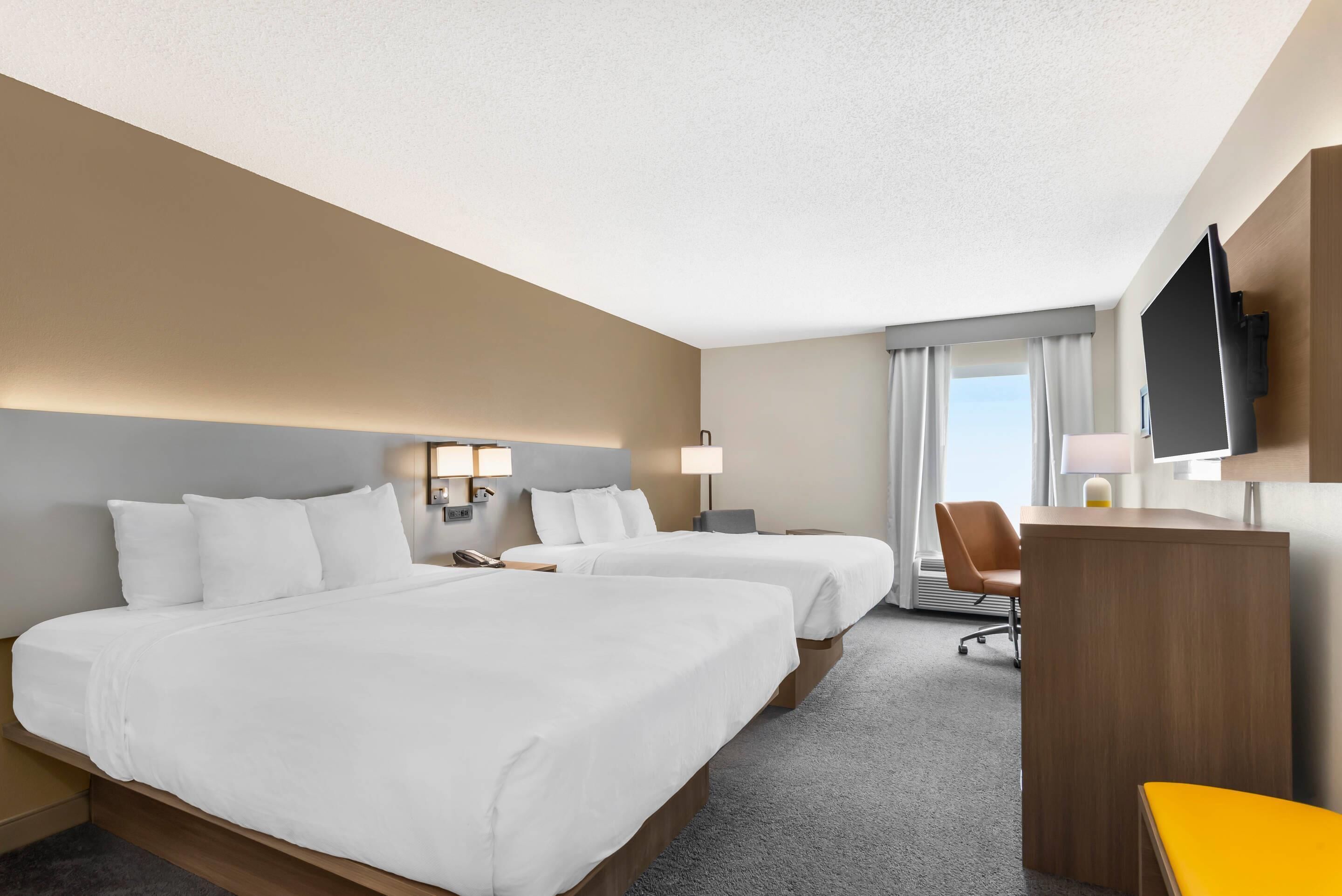 A hotel room with two beds, a desk, a chair, a TV, and a window with curtains.