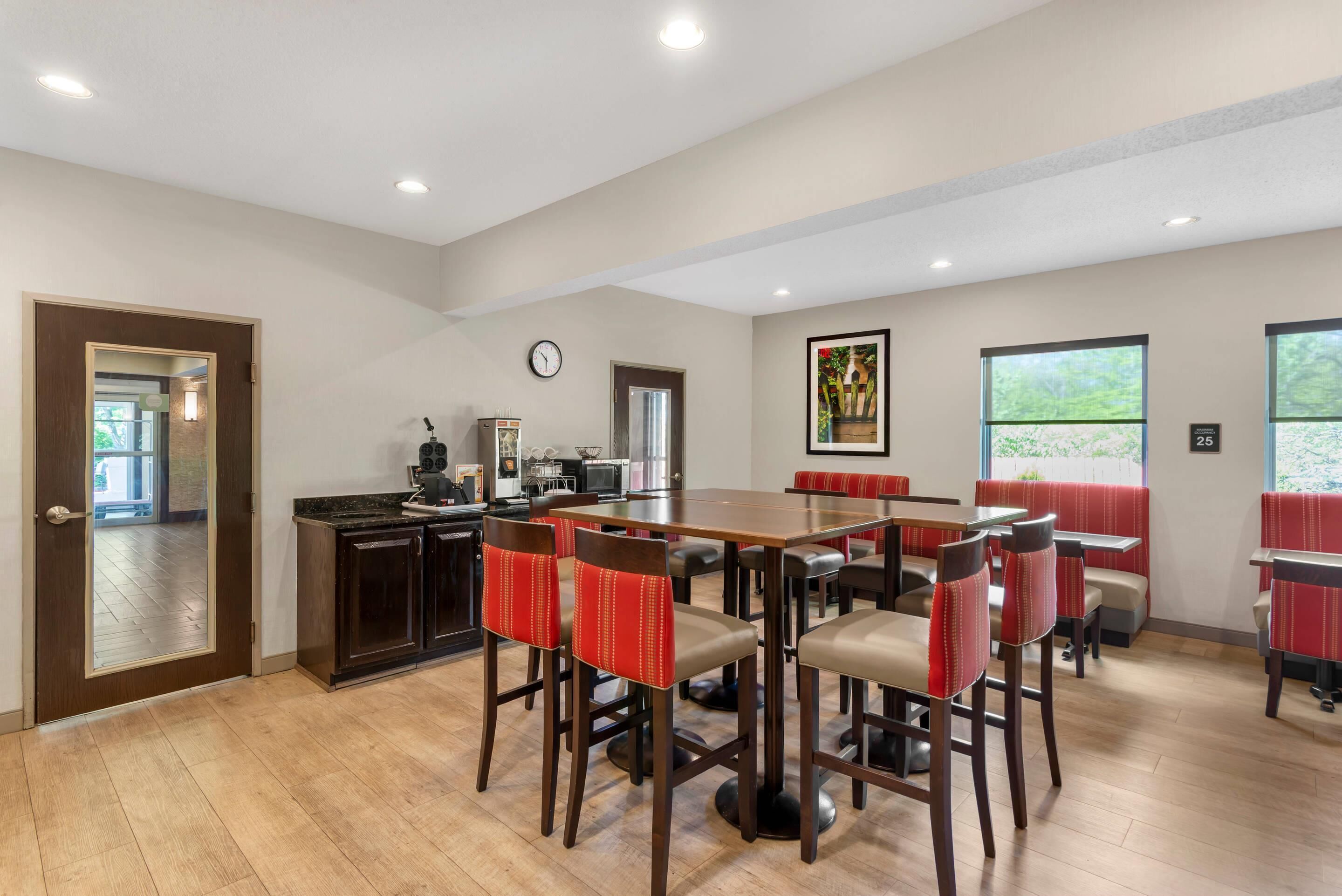 A dining area with wooden flooring, a large table, and red upholstered chairs.