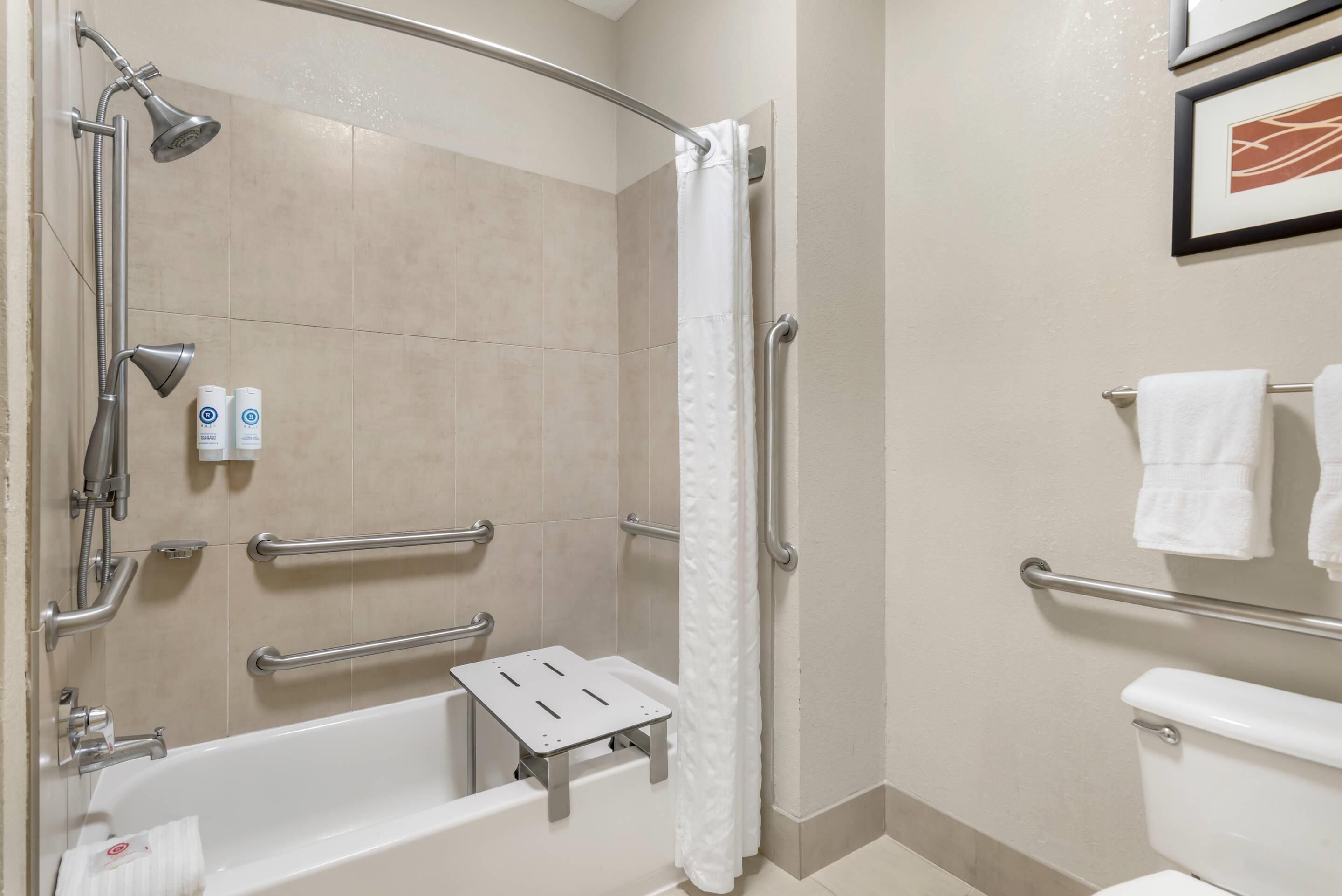 Un baño moderno con ducha, barras de apoyo, inodoro y toallero.