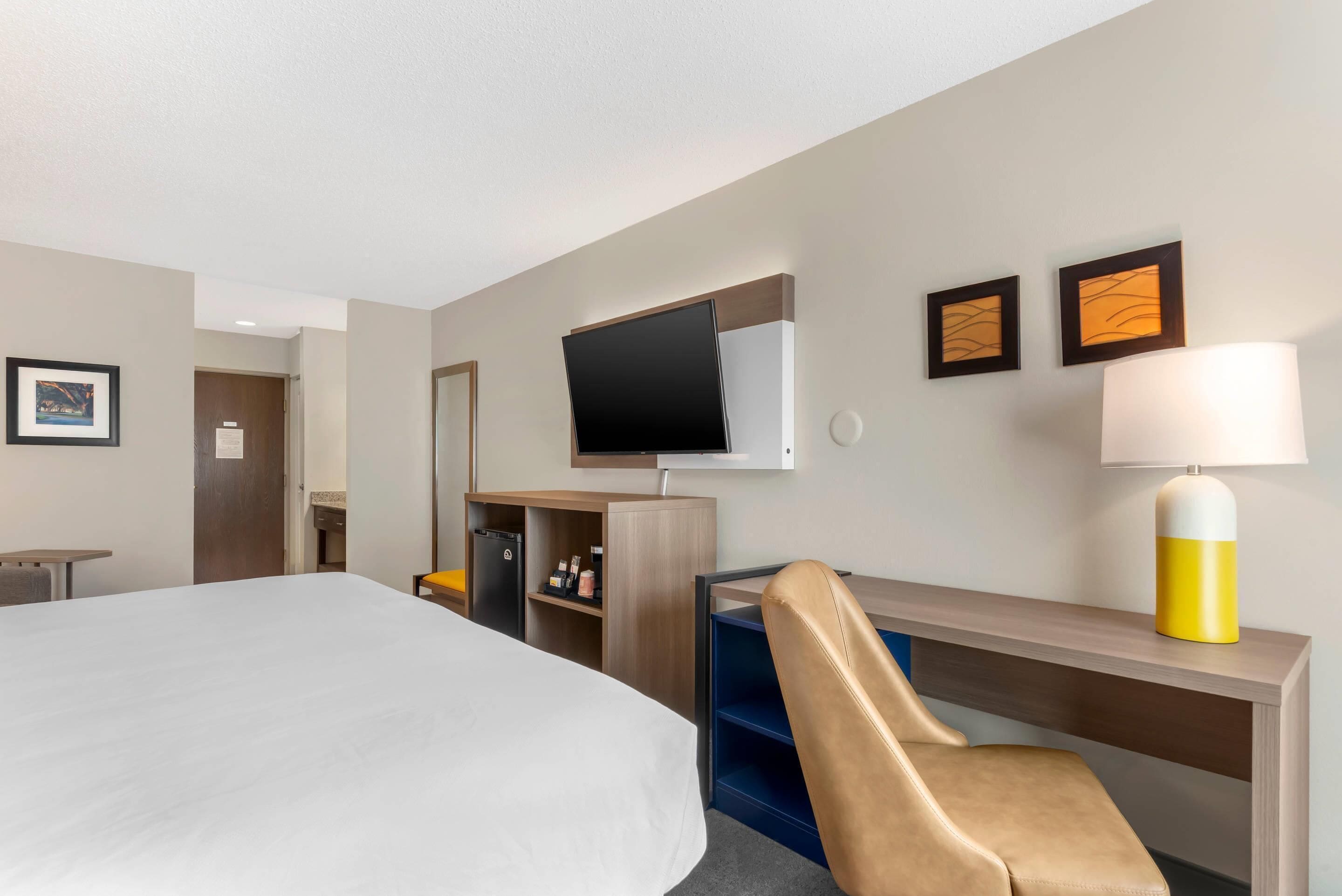 A hotel room with a bed, a desk, a chair, a TV, a lamp, and a wardrobe.
