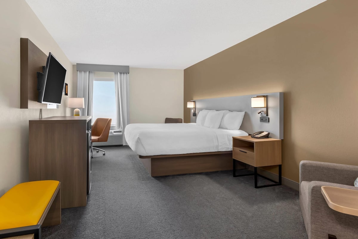 A hotel room with a bed, desk, chair, and TV.