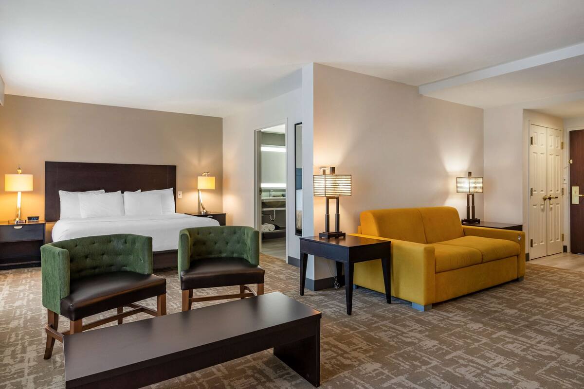 A hotel room with a bed, two armchairs, a sofa, a table, and two lamps.