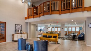 A spacious lobby with a yellow sofa, blue cylindrical stools, a wooden staircase, and a dining area with a table and chairs. - Best Western Plus Dalton Inn (Dalton)