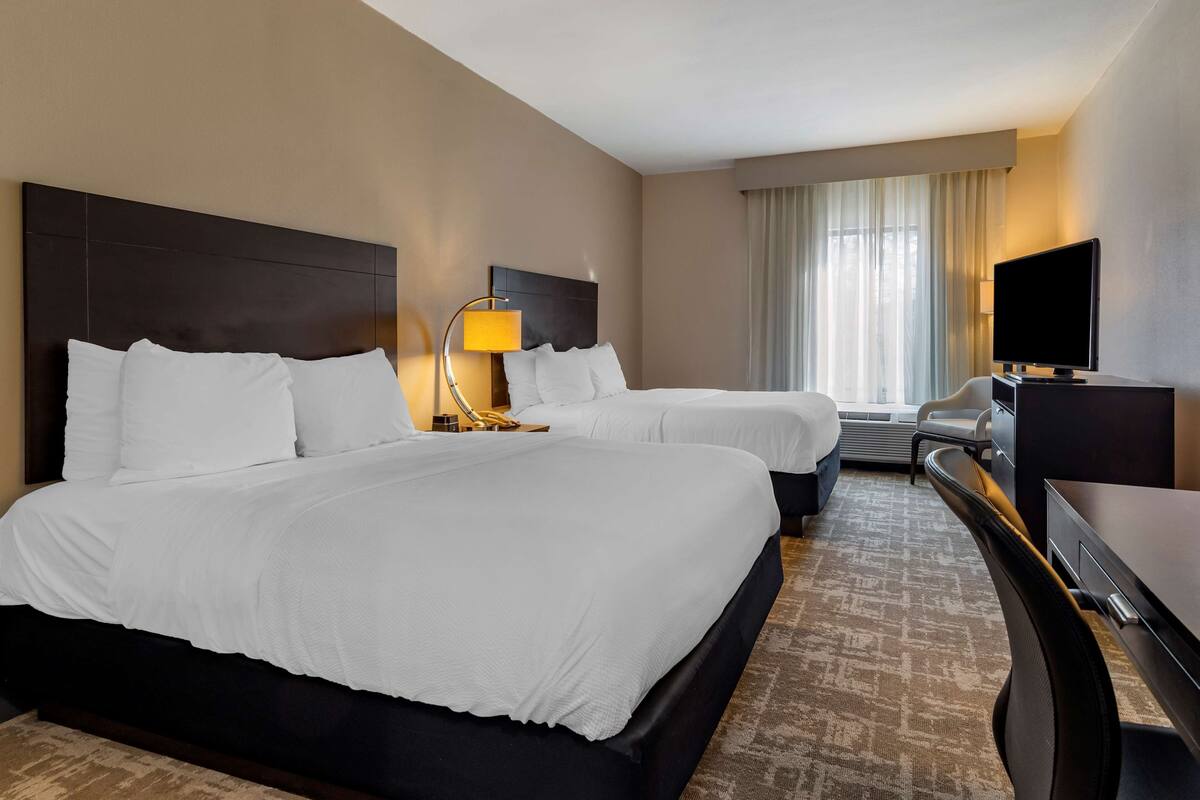 A hotel room with two beds, a desk, a television, and a lamp.