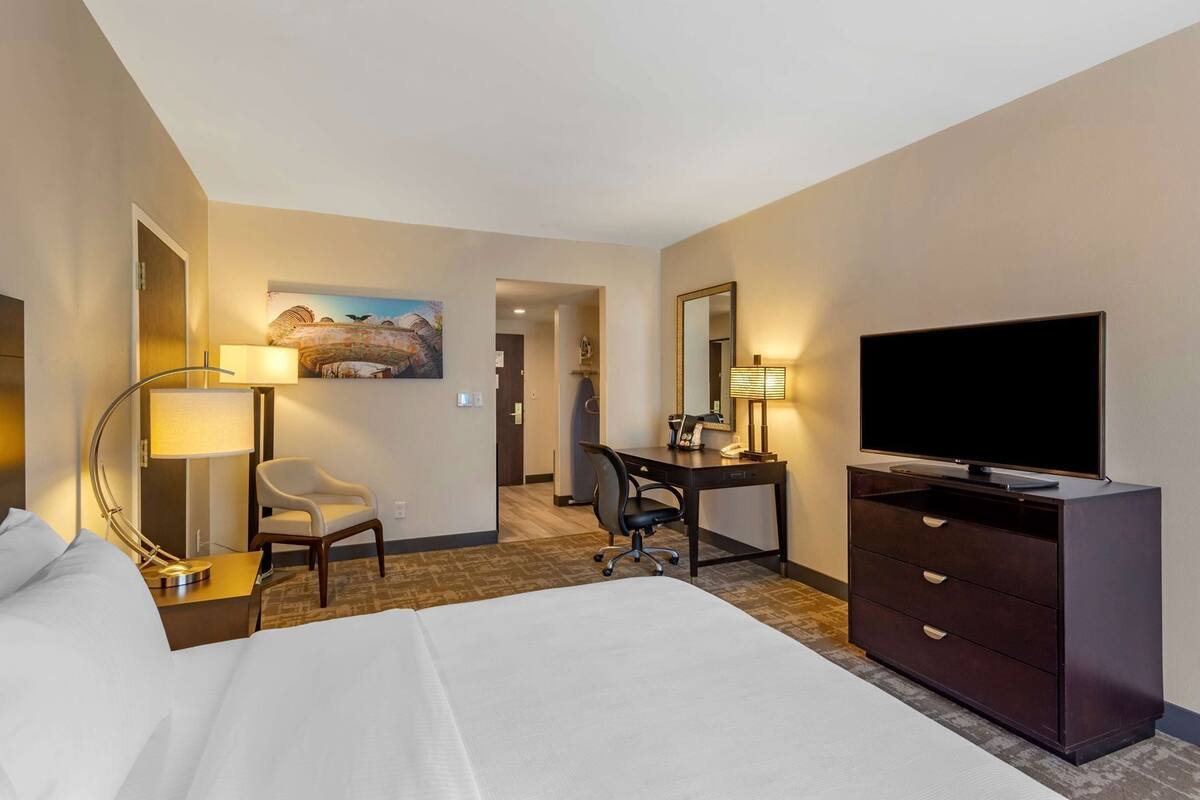 A hotel room with a bed, desk, chair, television, and a painting on the wall.