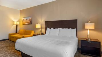 Una camera d'albergo con un letto grande, un divano, un comodino con una lampada e un quadro appeso al muro.