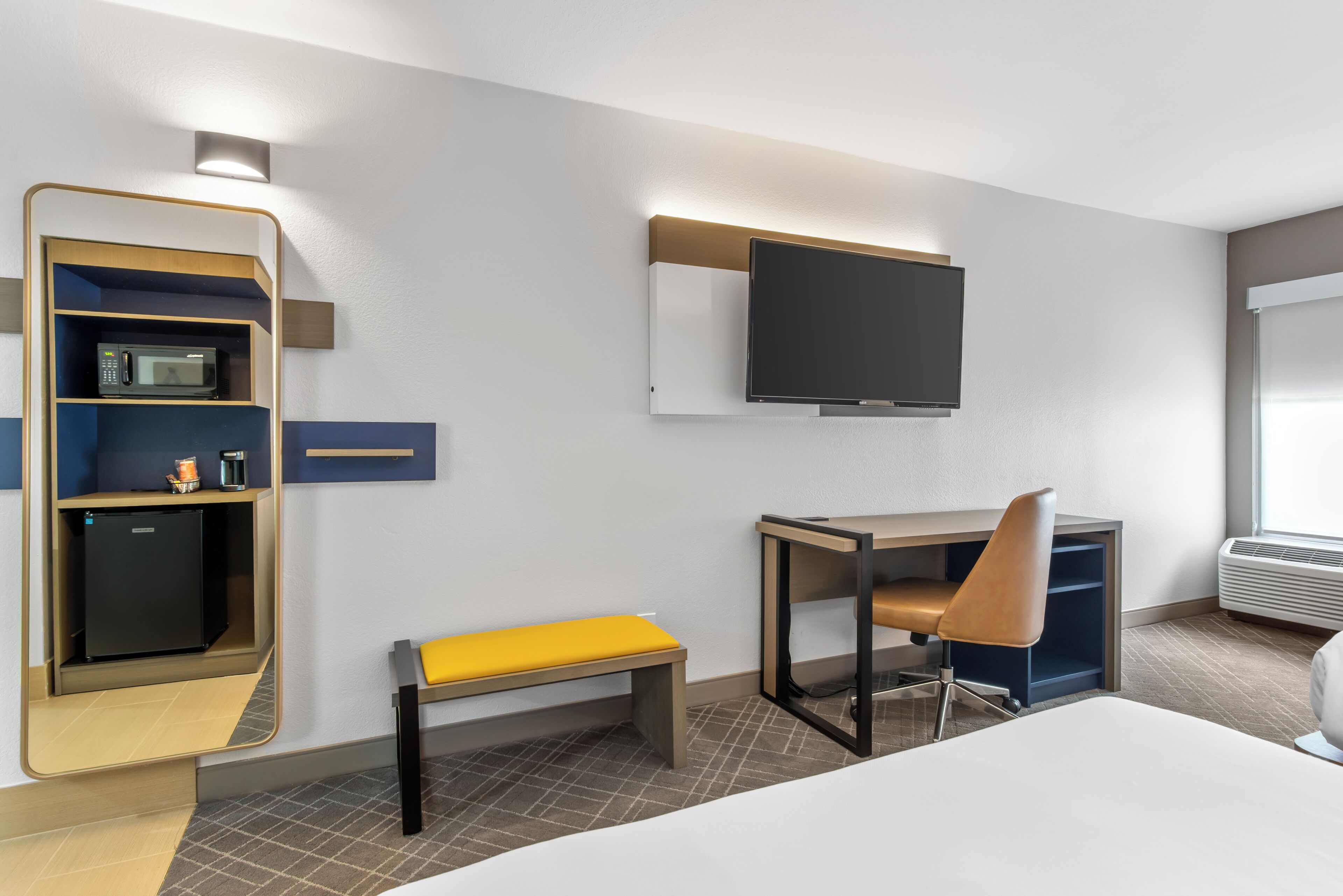 Een hotelkamer met een bed, een bureau met stoel, een televisie, een magnetron en een kleine koelkast.