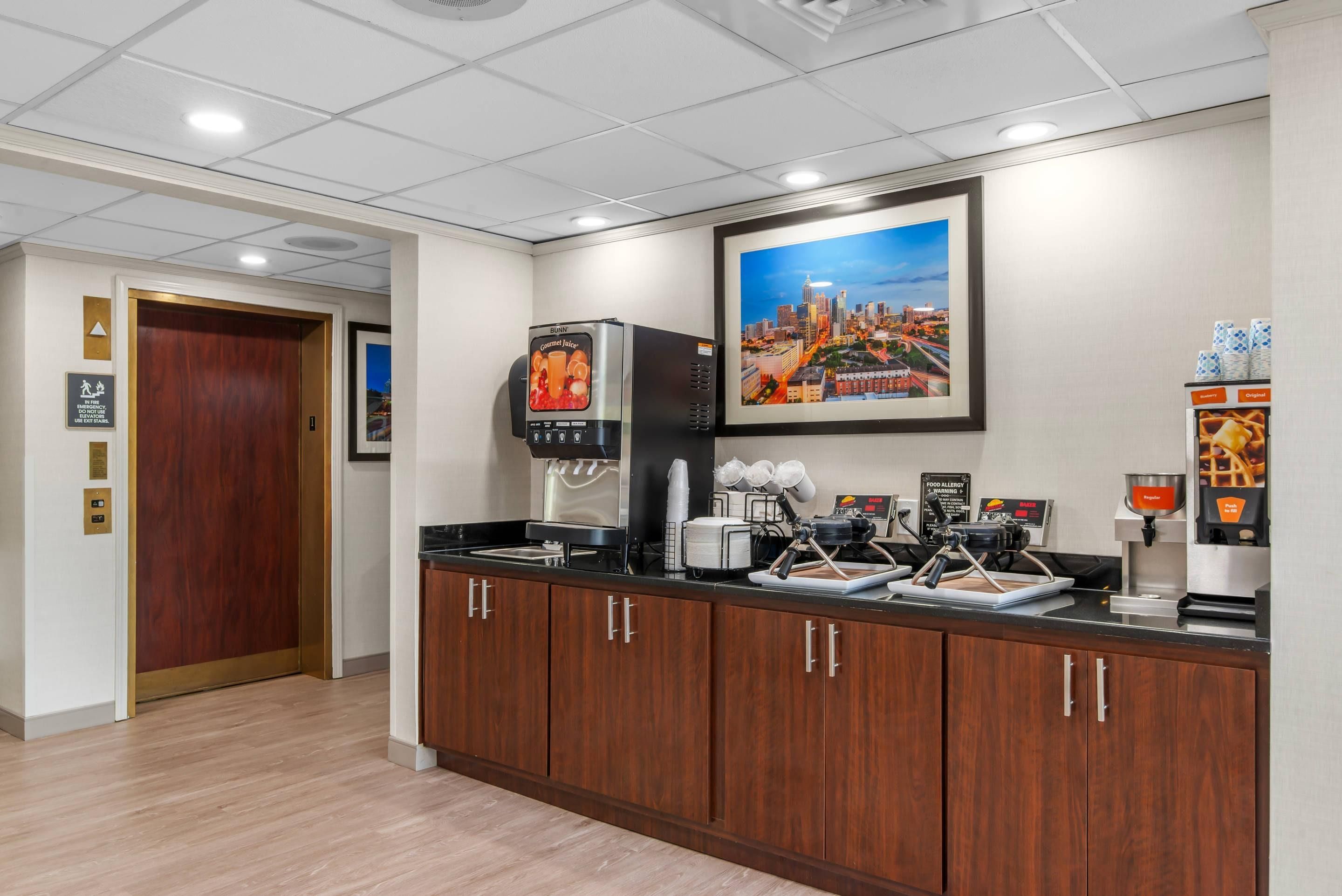 A hotel lobby with a coffee station, a framed cityscape picture, and a wooden door.