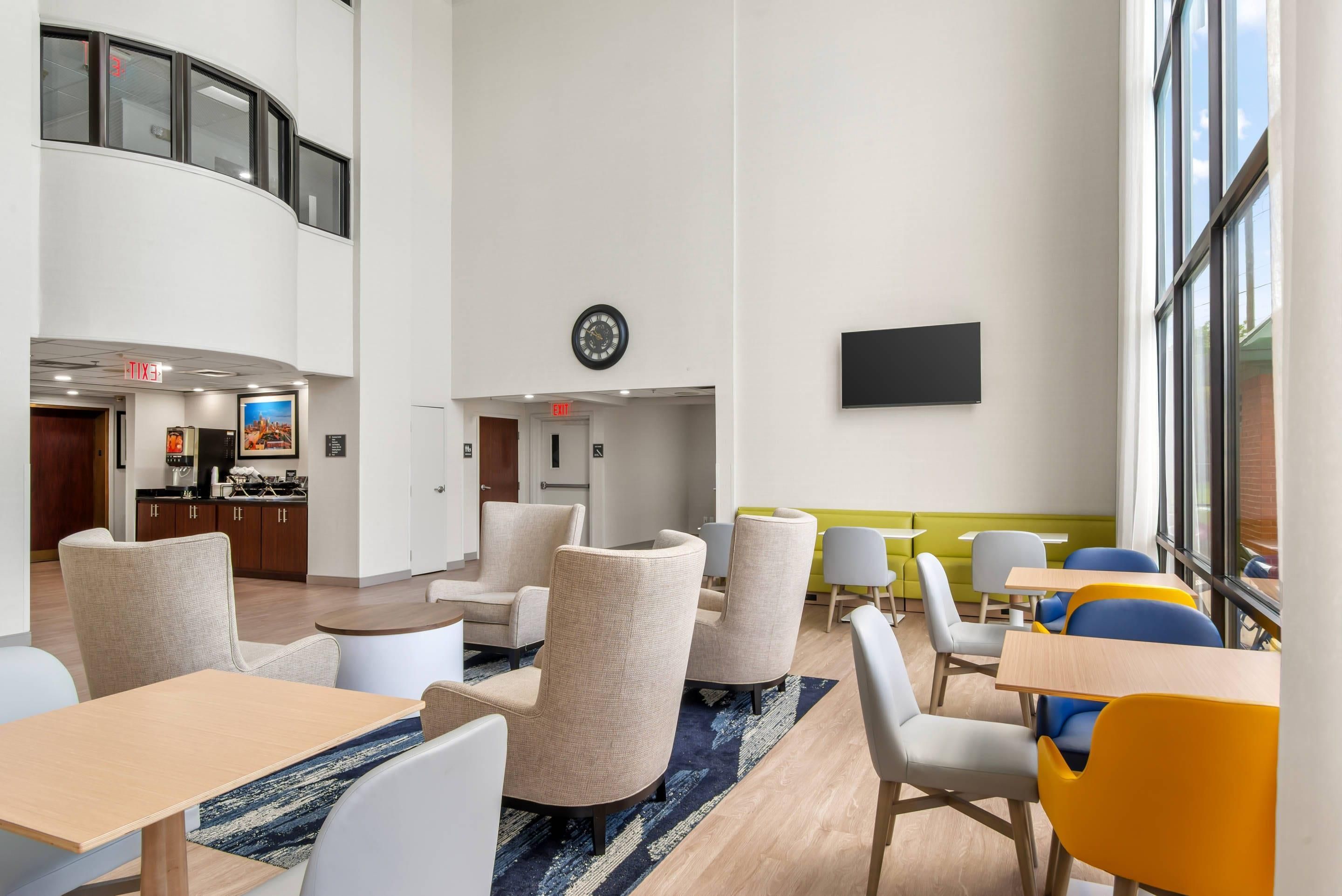 En hotelllobby med sittgrupper, en klocka, en platt-TV och ett kök synligt i bakgrunden.