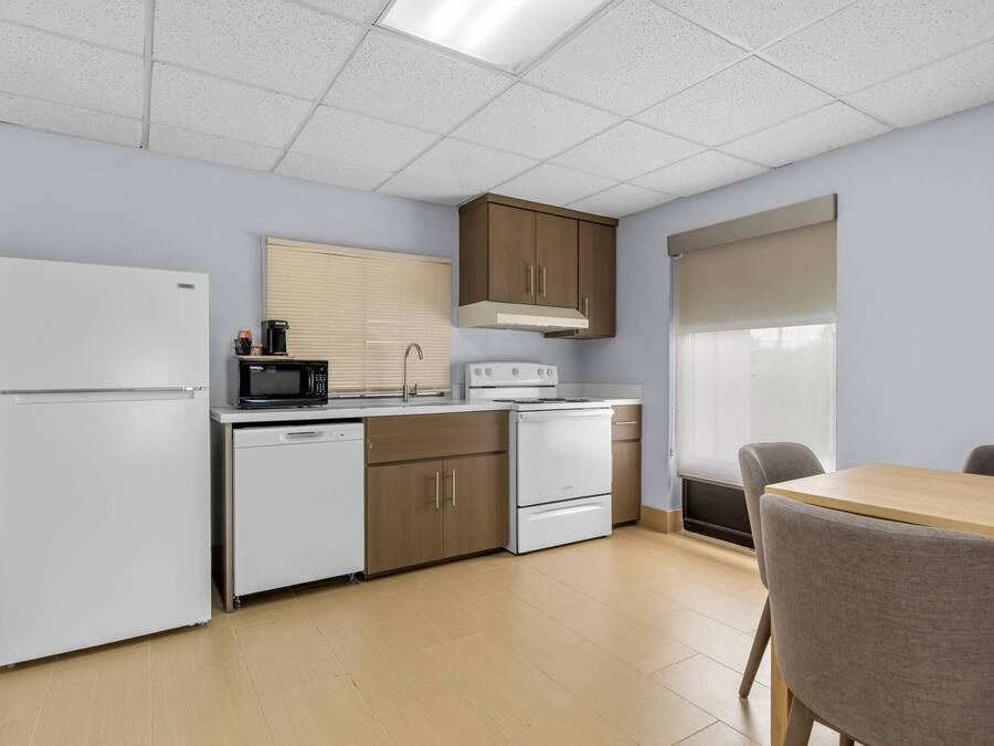 A modern kitchen with a refrigerator, microwave, stove, and dishwasher. There is a dining table with chairs and a window with blinds.