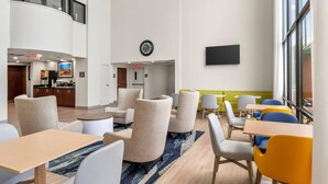 Eine Hotelhalle mit Sitzbereichen, einer Uhr, einem Flachbildfernseher und einer Küche im Hintergrund.