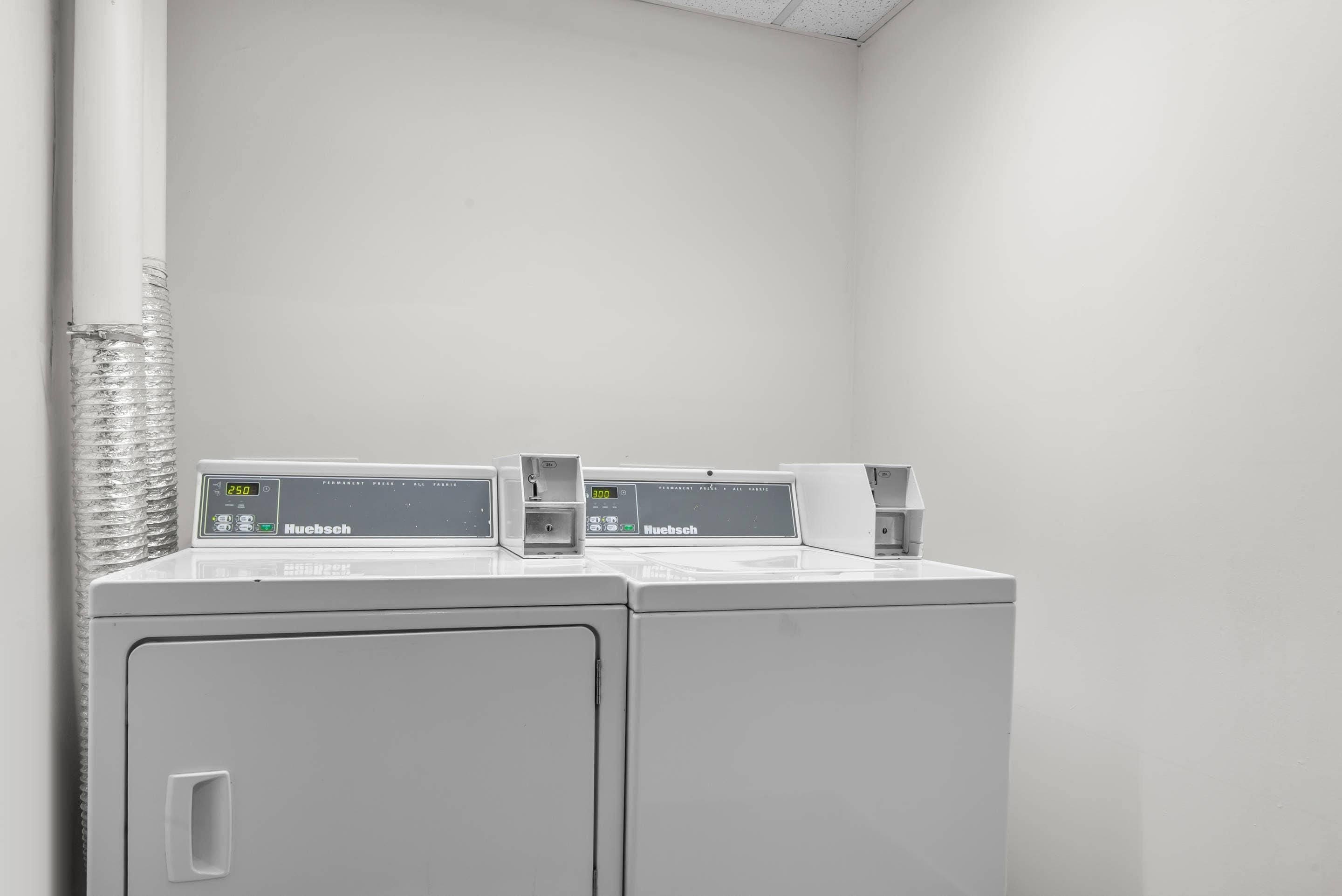 A laundry area with two white washing machines and a dryer, both labeled 'Huebsch.'