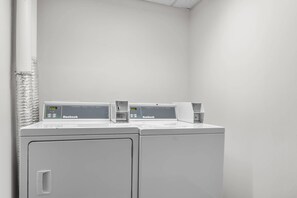 A laundry area with two white washing machines and a dryer, both labeled 'Huebsch.' - Comfort Inn Douglasville - Atlanta West (Douglasville)