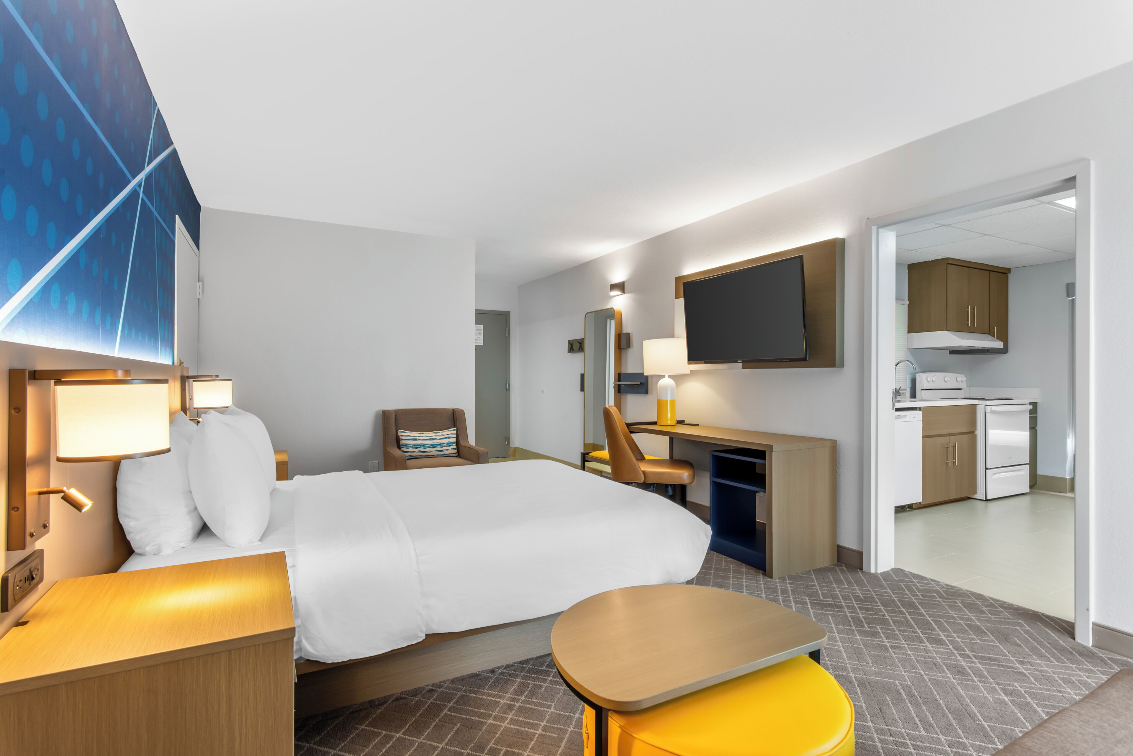 A hotel room with a bed, desk, chair, and a small kitchenette.