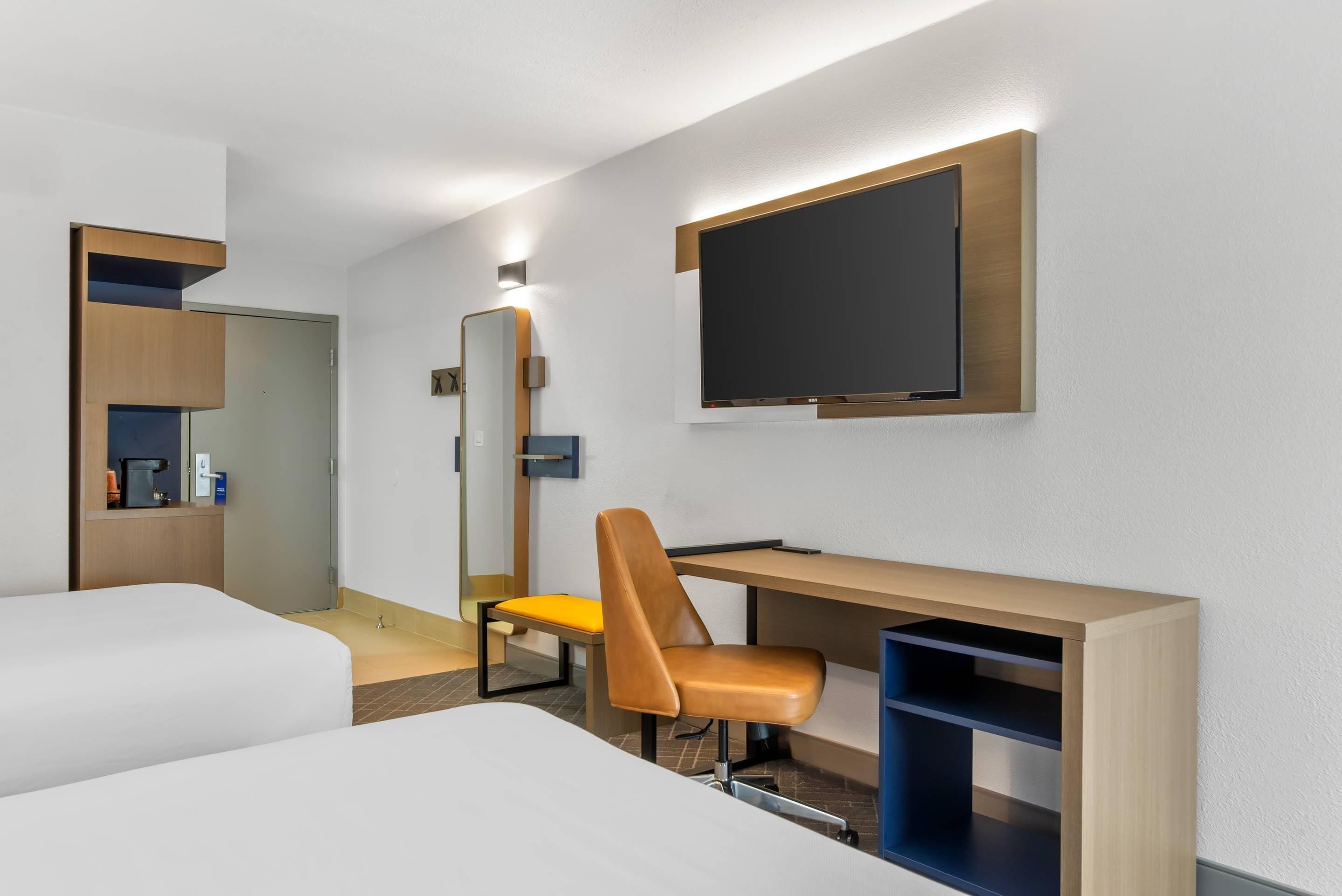 A hotel room with two beds, a desk with a chair, a TV, a mirror, and a coffee machine.