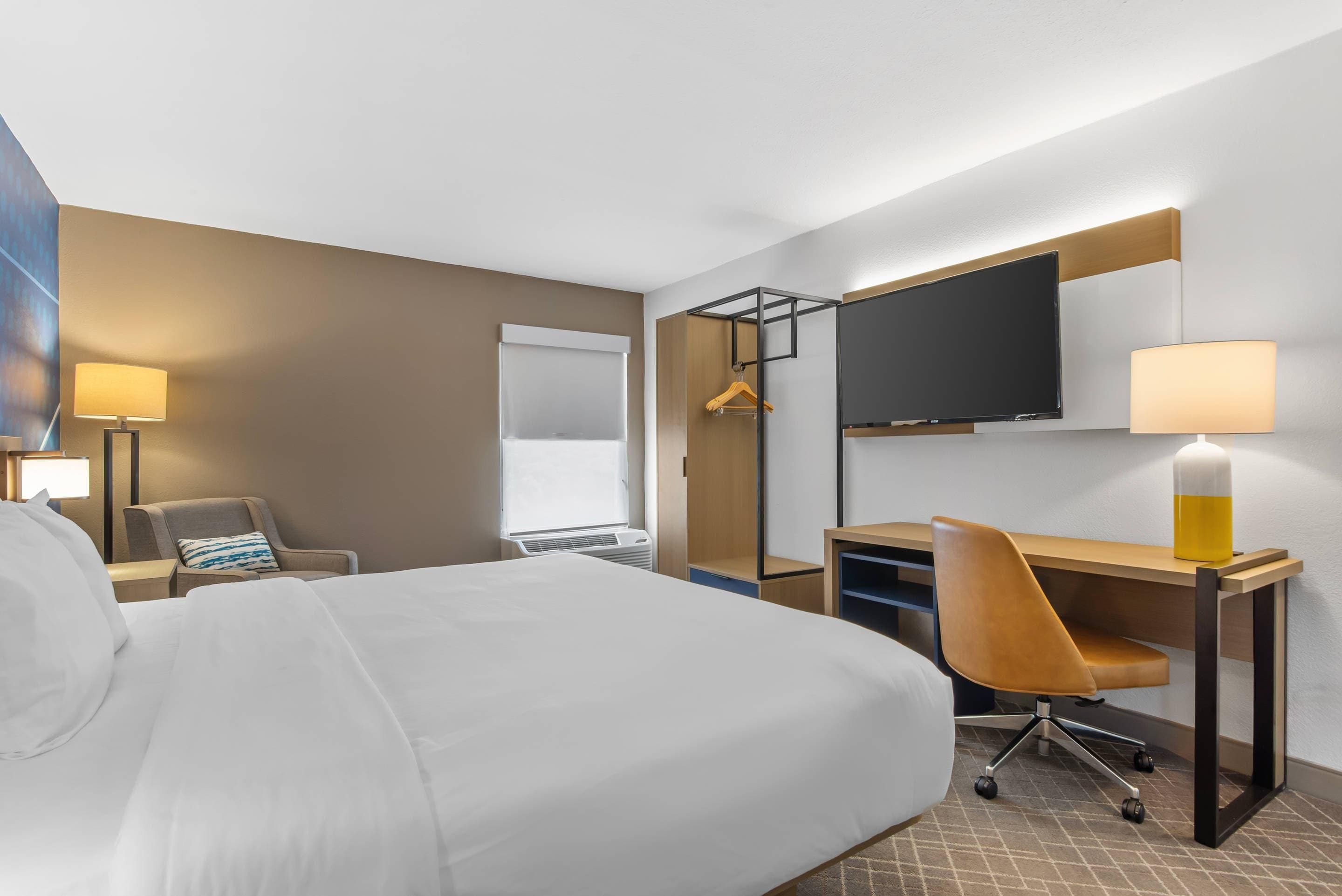 A hotel room with a bed, desk, chair, TV, and a window.